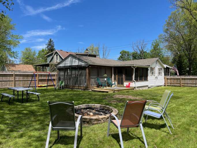 Backyard Basking Beneath Blue Skies, Chairs Circled Around A Fire Pit
