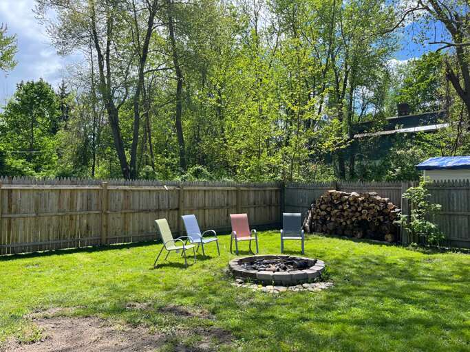 Fenced Garden With Chairs Arranged Around A Fire Pit, Woodpile Nearby
